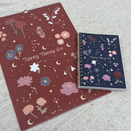 Two planners with floral and celestial designs on a textured surface