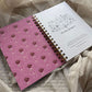 Spiral-bound notebook with pink rose pattern on cover, placed on a textured surface.