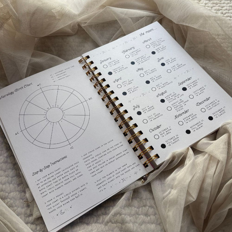 Open spiral-bound notebook with celestial chart and text on a soft fabric background