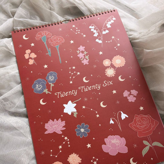 Red calendar with floral designs and 'Twenty Twenty Six' text on a light fabric background