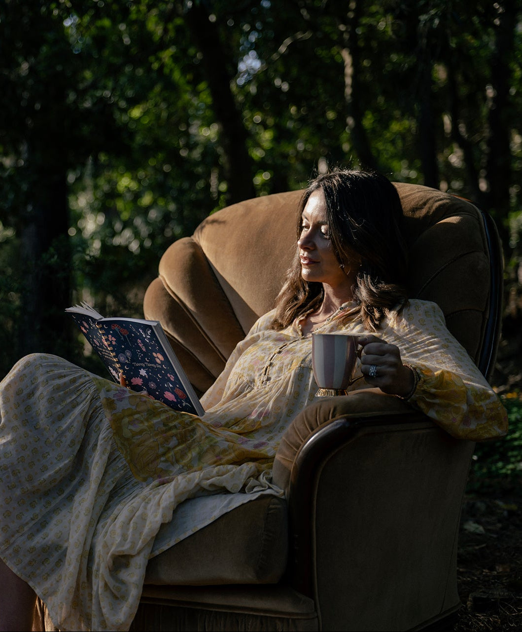 Woman sitting in a chair outdoors, holding a diary and a mug.