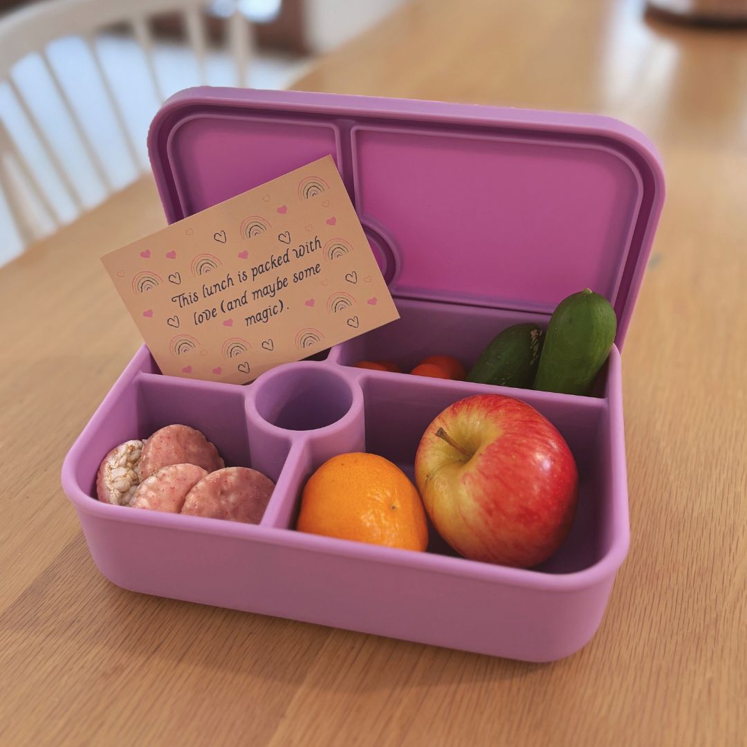 Purple bento box with snacks on a wooden table with an affirmation card in it.